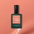 A bottle of Manucurist Green Flash gel polish in Peach rests on a peach background with a painted white swoosh underneath. The label highlights instant dry and extra long wear, making it an ideal summer tint.