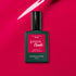 A bottle of Manucurist Péonie Green Flash gel polish rests on a glossy, bright pink surface reflecting light.