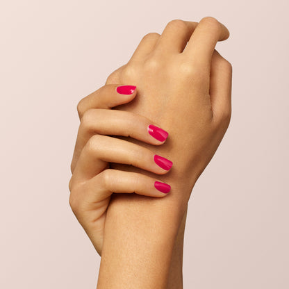 A close-up of two hands with neatly manicured nails painted in Péonie by Manucurist, a vibrant raspberry pink shade, set against a soft beige background.