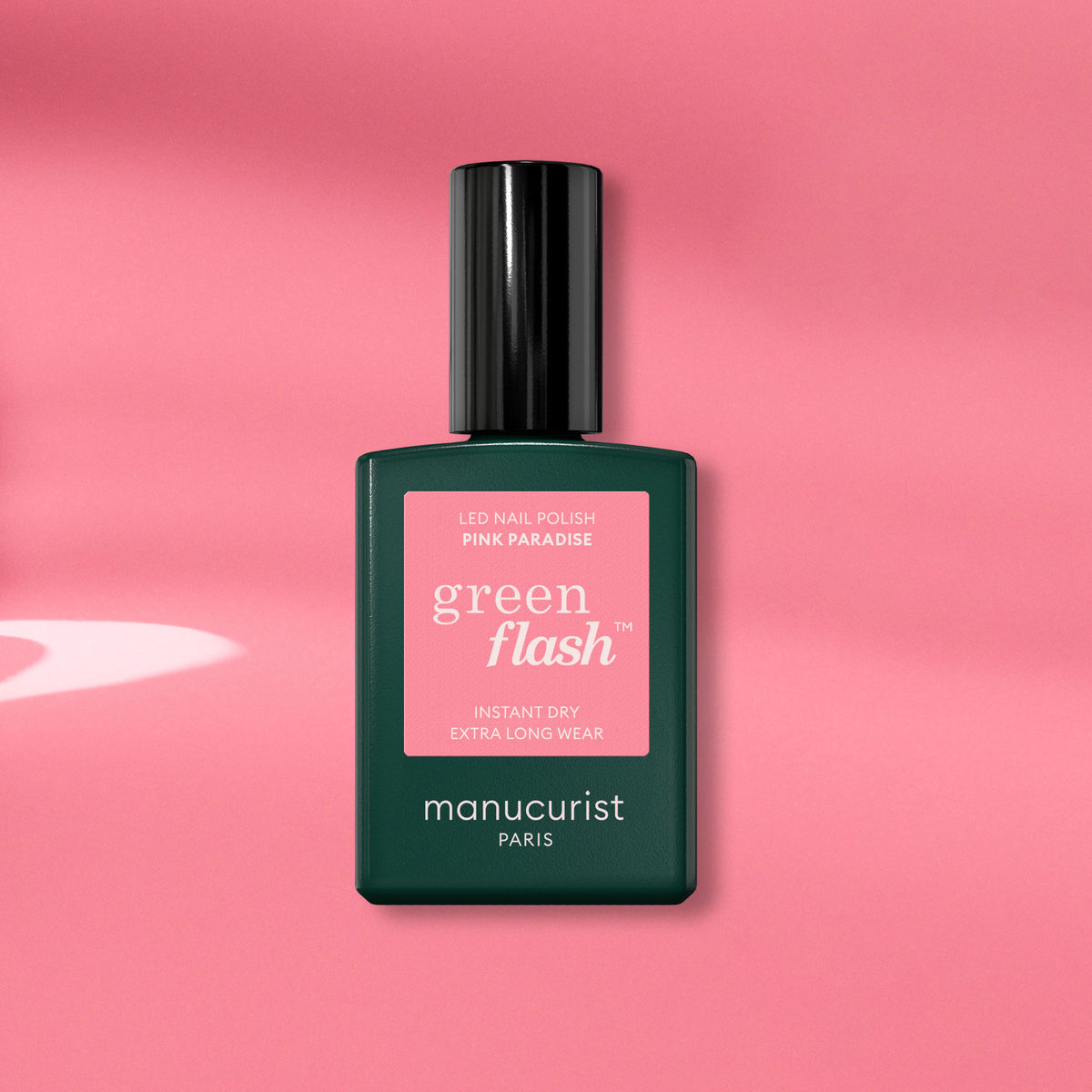 A Manucurist Pink Paradise Green Flash gel polish bottle, with a dark green base and black cap, is displayed on a pink background with soft shadows.