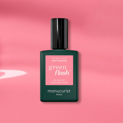 A Manucurist Pink Paradise Green Flash gel polish bottle, with a dark green base and black cap, is displayed on a pink background with soft shadows.