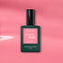 A Manucurist Pink Paradise Green Flash gel polish bottle, with a dark green base and black cap, is displayed on a pink background with soft shadows.