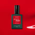 A bottle of Manucurist Poppy Red gel polish with a black cap rests on a bold red background, casting a dramatic shadow.
