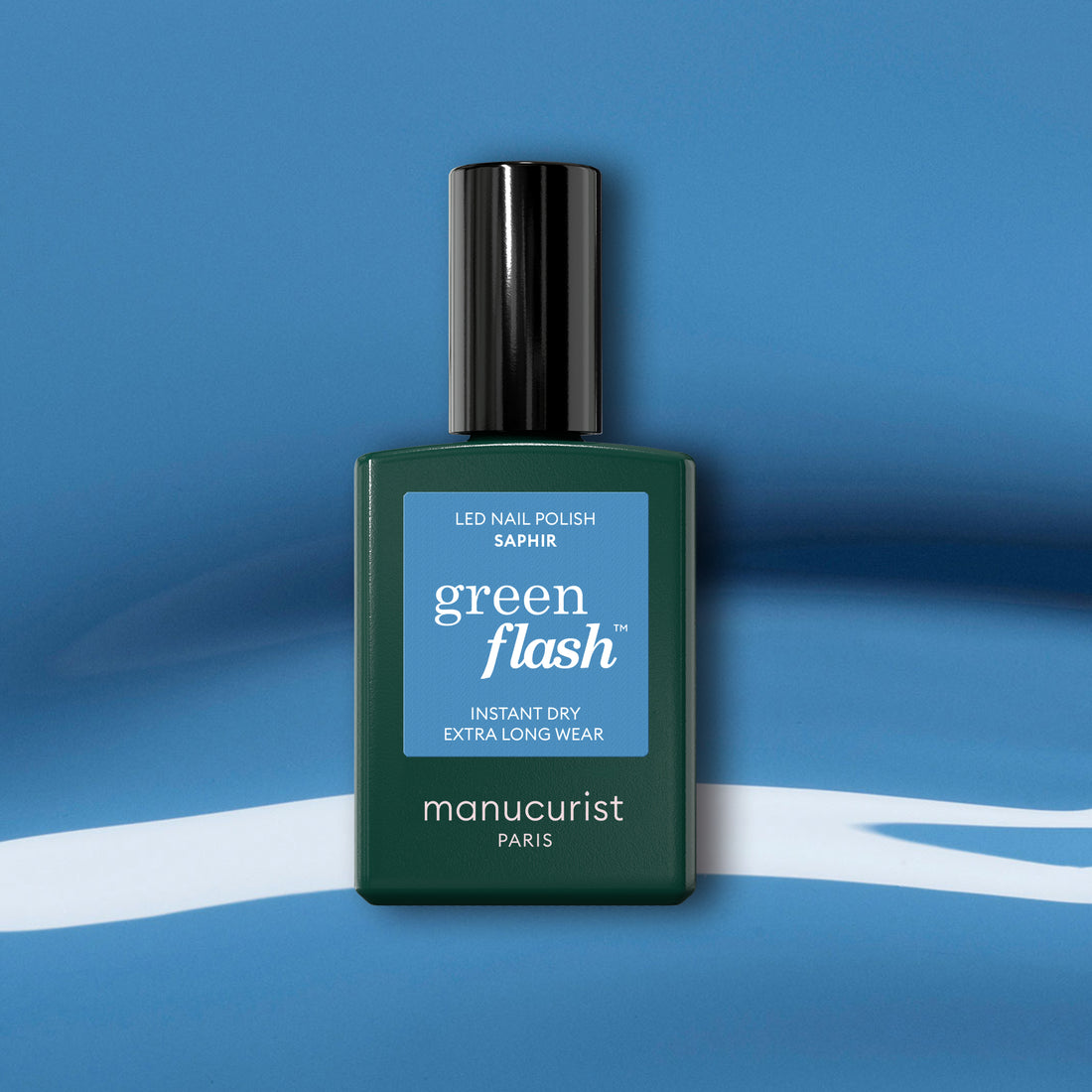 A Manucurist Saphir gel polish bottle with a black cap is displayed on a blue and white abstract background.