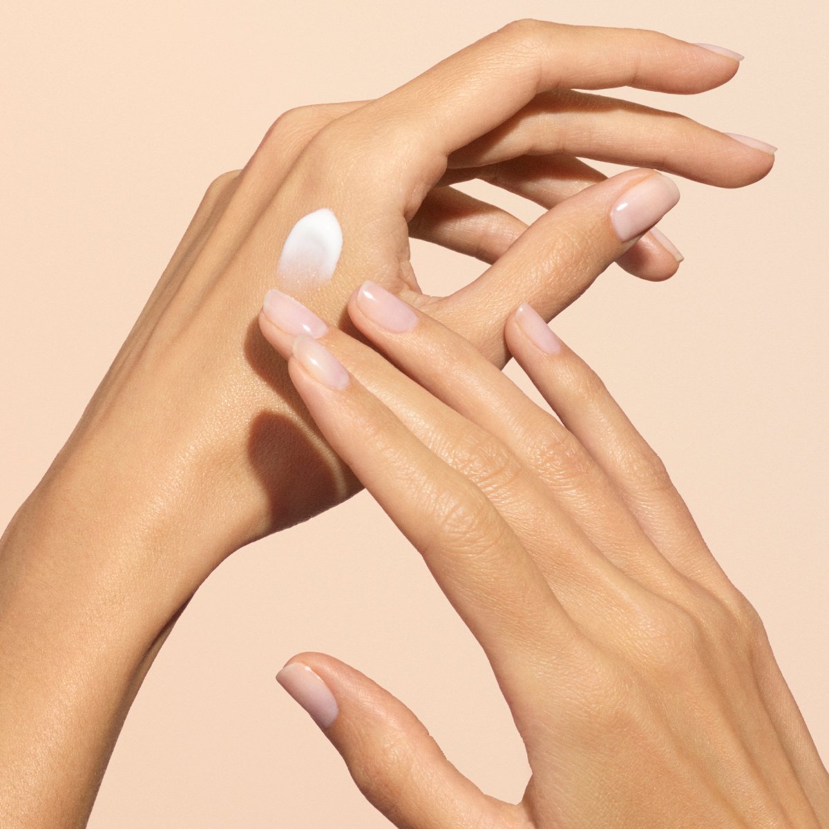 Gros plan sur deux mains aux ongles manucurés nude appliquant délicatement la Crème Mains Everyday Orange Blossom de Manucurist - Cosmos Organic sur le dos d&