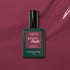 A bottle of Manucurist Victoria Plum gel polish sits on a matching plum background. The sleek dark green bottle has a maroon label and black cap, perfectly highlighting this rich plum shade.